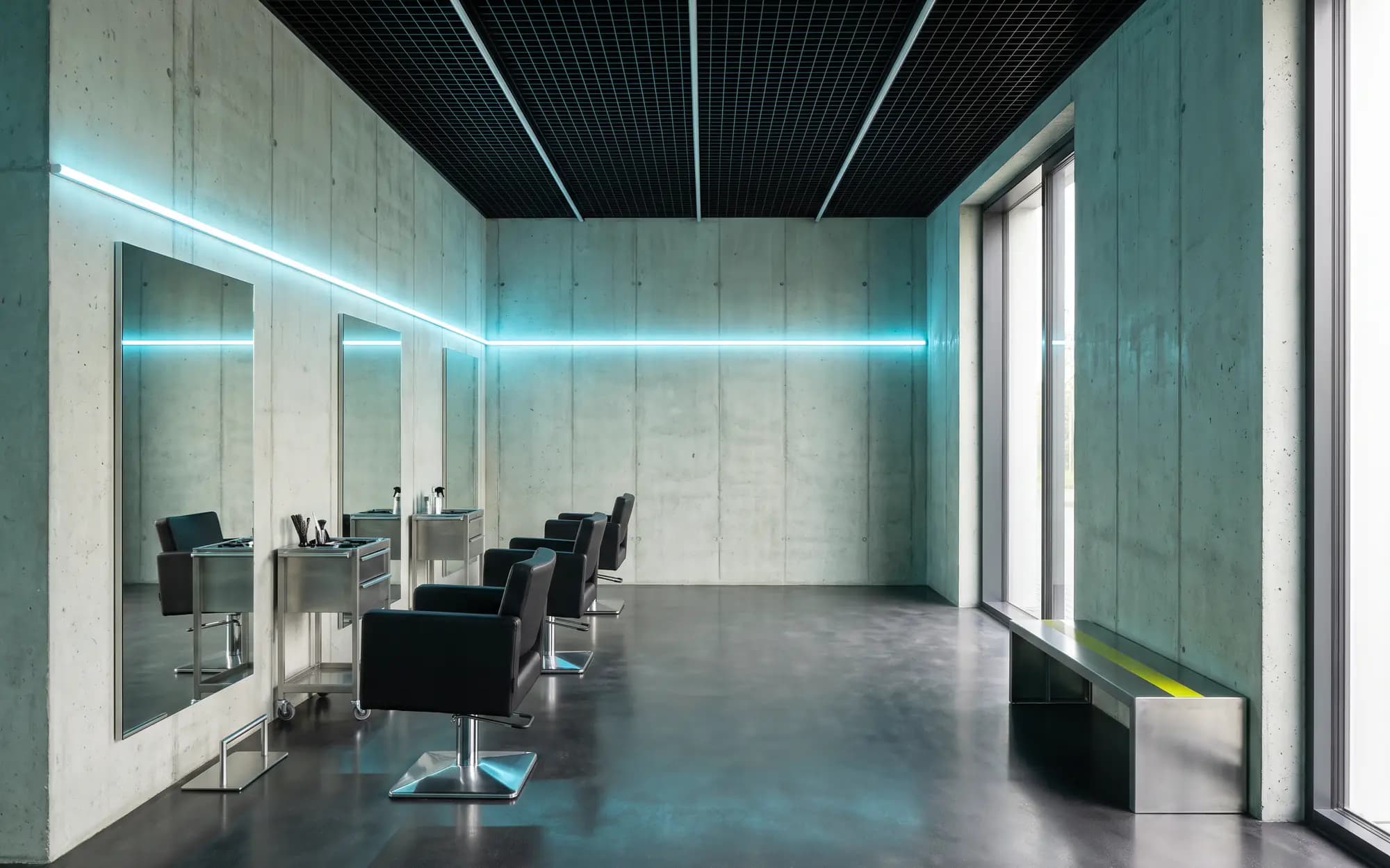 Ein moderner Friseursalon: Betonwände, schwarze Stühle vor bodenhohen Spiegeln und ein durchgehendes türkisfarbenes Lichtband. Symbolbild, nicht der Salon von Hair Freaks.